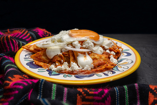 Traditional mexican red chilaquiles with fried egg on dark background