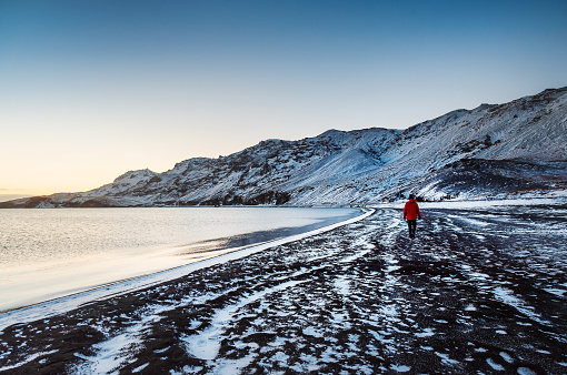 Male traveler visiting Kleifarvatn lake in Iceland with amazing snow covered mountain scenery during winter at sunset