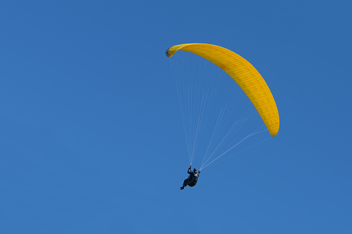 Paraglider pilot with a yellow glider is flying in the clear blue sky, recreational and competitive adventure sport, copy space