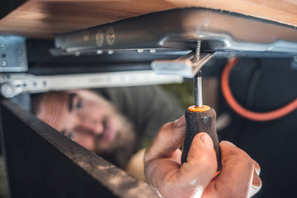 Man using a small screwdriver in a confined space Underneath a kitchen counter of a camper van. A young man is installing the gas stove. confined space stock pictures, royalty-free photos & images