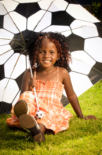 Portrait of young South African girl smiling, sitting under a soccer ball umbrella.