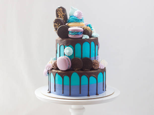 istock Tiered blue cake decorated with dark chocolate, cupcake, cookies, macaroons, meringues, popsicles and chocolate bars. 1249966573