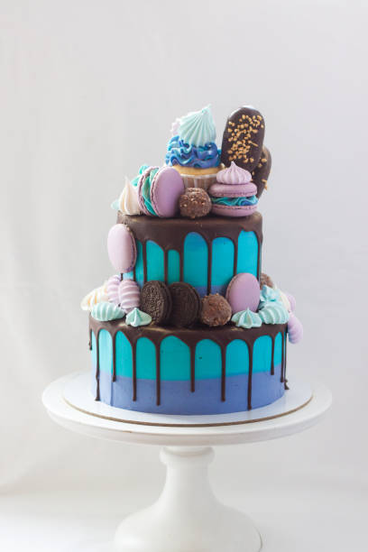 istock Tiered blue cake decorated with dark chocolate, cupcake, cookies, macaroons, meringues, popsicles and chocolate bars. 1249966590