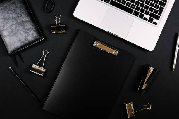 istock Top view of a workspace with laptop computer keyboard, notebook, pen, clipboard and clips on black background. Close up, copy space, background, flat lay 1249967531