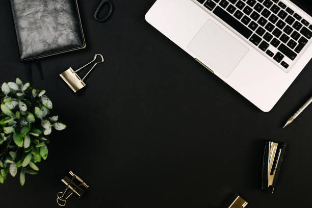 istock Top view of a workspace with laptop computer keyboard, office plant, notebook, pen, clipboard and clips on black background. Close up, copy space, background, flat lay 1249967560