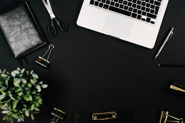 istock Top view of a workspace with laptop computer keyboard, office plant, notebook, pen, clipboard and clips on black background. Close up, copy space, background, flat lay 1249967575