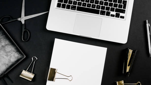 istock Top view of a workspace with laptop computer keyboard, notebook, pen, clipboard and clips on black background. Close up, copy space, background, flat lay 1249967577