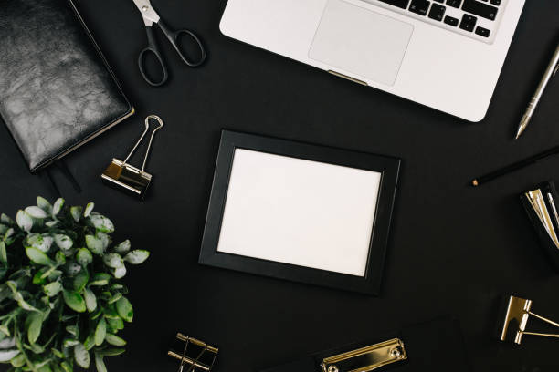 istock Top view of a workspace with laptop computer keyboard, frame, office plant, notebook, pen, clipboard and clips on black background. Close up, copy space, background, flat lay 1249967598