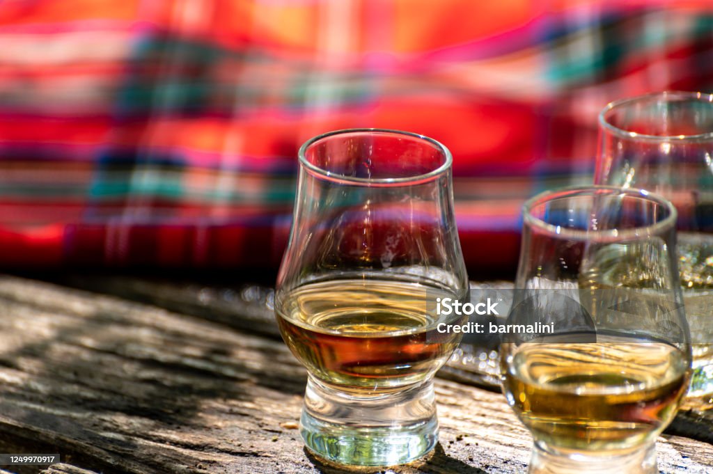 Tasting of different Scotch whiskies on outdoor terrace, dram of whiskey and red tartan Tasting of different Scotch whiskies on outdoor terrace, dram of whiskey and red tartan close up Whiskey Stock Photo