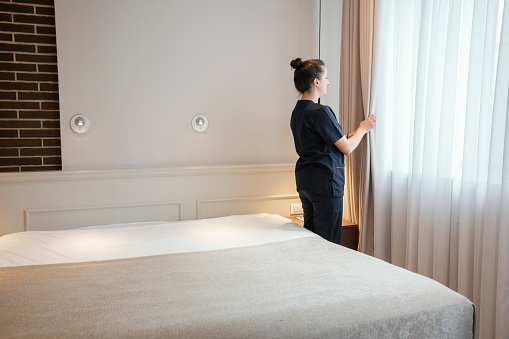 Maid doing the curtain, preparing hotel room for guests
