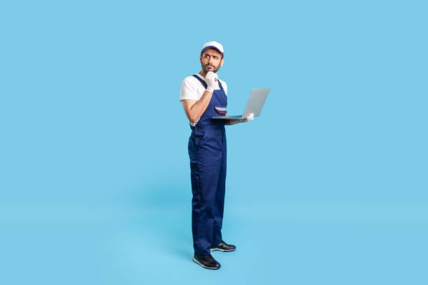 istock Full length thoughtful uncertain workman in uniform and protective gloves holding laptop, pondering decision 1249972843