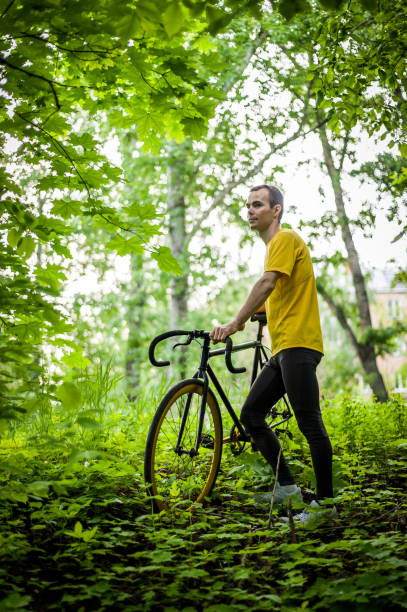A young Man stopped to rest With his Bicycle in a public Park. He enjoys an early Sunny morning in the forest.