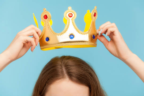 Closeup of woman putting on head golden crown, concept of awards ceremony, privileged status, superior position Closeup of woman putting on head golden crown, concept of awards ceremony, privileged status, superior position, self-motivation and big ambitions to achieve success. indoor studio shot, isolated coronation photos stock pictures, royalty-free photos & images