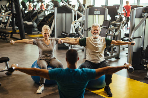 istock Senior couple exercising with personal trainer using dumbbells at the gym 1249978324