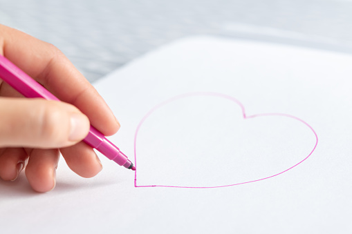 Woman with a marker draws a red heart on a white sheet of paper. International Lefthanders Day
