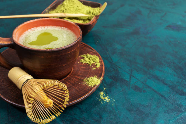 istock Close up green matcha tea, whisk and powder in brown ceramic cups on emerald backdrop. Copy space for text. 1249982687