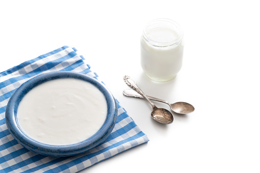 Homemade yogurt blue bowl and glass container with vintage spoons isolated on white background