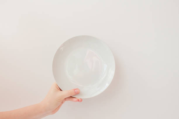 istock Female hand holds a white round plate on a white background as a mockup with copy space. Ceramic flat saucer 1249982767