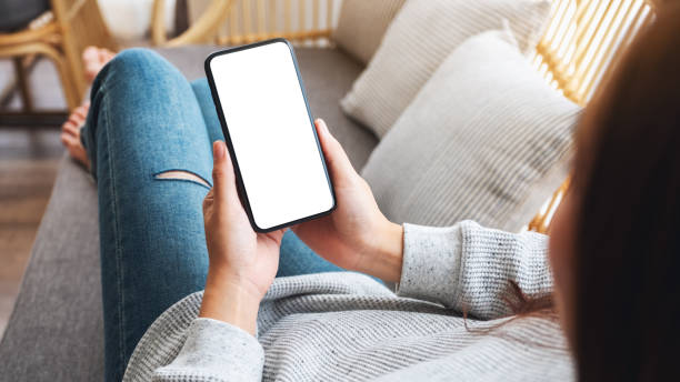 istock a woman holding mobile phone with blank desktop white screen while lying on a sofa at home 1249985828