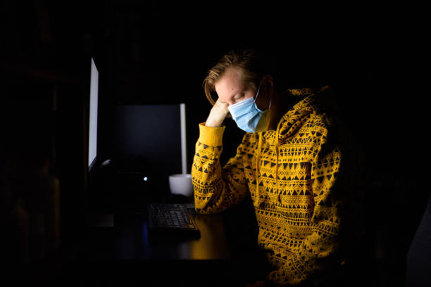 istock Stressed young man with mask looking tired while working from home late at night in the dark 1249990305