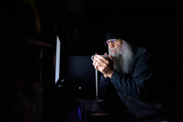 istock Mature bearded hipster man drinking coffee while working overtime at home late at night in the dark 1249990541