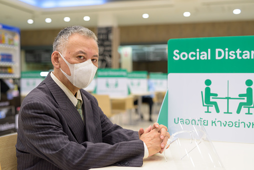 Portrait of mature Japanese businessman with mask for protection from corona virus outbreak social distancing at the food court