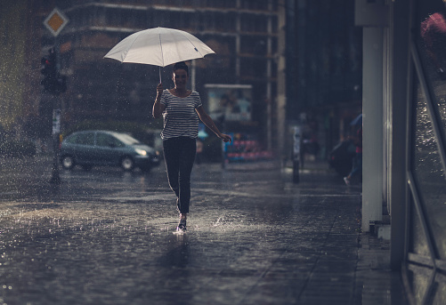 Full length of happy woman holding umbrella and running on the rain.