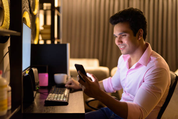 istock Happy young Indian businessman using phone while working overtime at home 1249994392