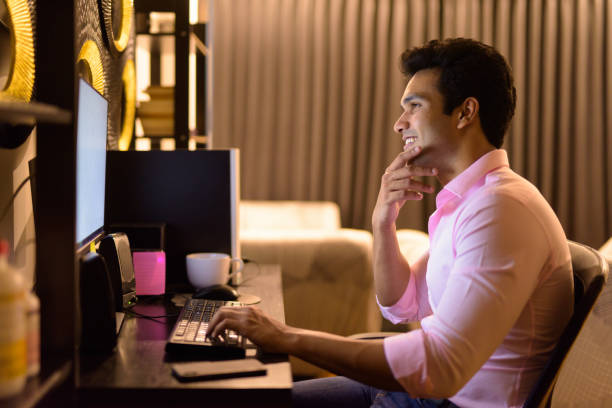 istock Happy young handsome Indian businessman thinking while working overtime at home 1249994448