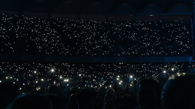Crowd waving cellphones and flashlights at stadium during rock concert / sports game