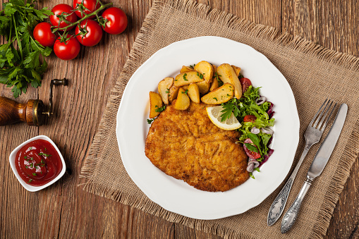 Chicken schnitzel, served with roasted potatoes and salad. Top view. Natural wooden background