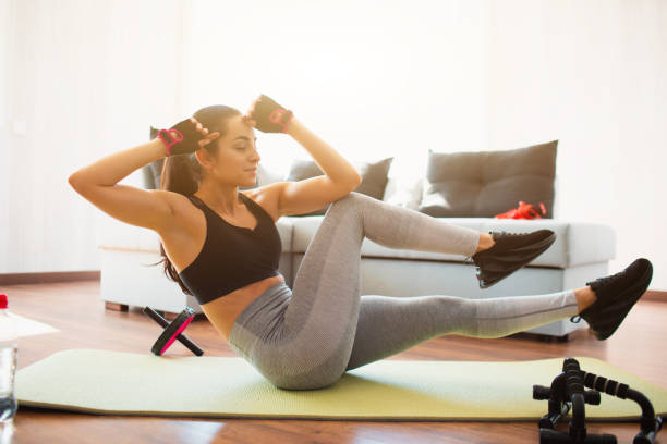 Young woman doing sport workout in room during quarantine. Cheerful lovely well built girl doing across hands and legs exercise. Touching knee with elbow. Doing abs workout at home una joven haciendo ejercicio deportivo en la habitación durante la cuarentena. alegre encantadora chica bien construida haciendo ejercicio a través de las manos y las piernas. tocar la rodilla con el codo. hacer entrenamiento de abdominales en casa.