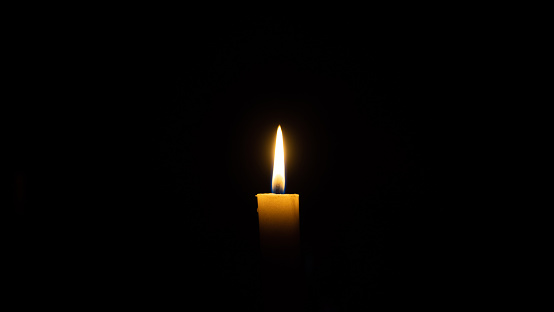 A candle burns in the darkness, copy space. A lit white candle on a black background. Symbol of eternal memory, mourning, minutes of silence, memorial day. The concept of loss and to the memory.