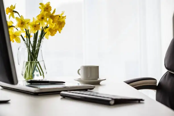 Photo of Shot of an tidy office desk with a bouquet of yellow daffodils for a pop of color