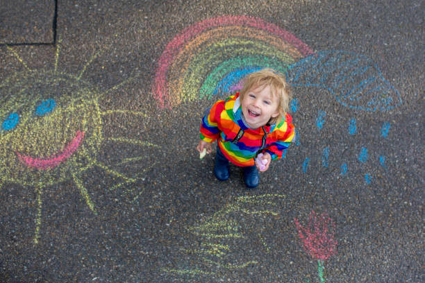 istock Cute toddler. playing in the rain with chalks, drawing on the asphalt, having fun 1250010435