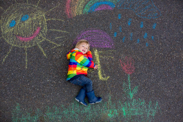 istock Cute toddler. playing in the rain with chalks, drawing on the asphalt, having fun 1250010469