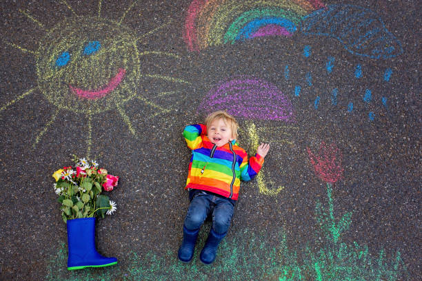 istock Cute toddler. playing in the rain with chalks, drawing on the asphalt, having fun 1250010504