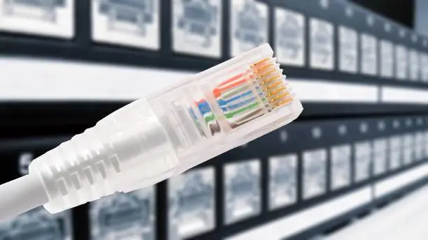 Conceptual shot of data connection with rj45 patch cable in foreground and panel with data ports in background.