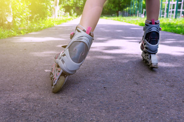 Unrecognizable Caucasian Teenager girl roller skating in the park. Sunset time. Close up. Rollerblades. Rear view of children's legs in roller skates.
