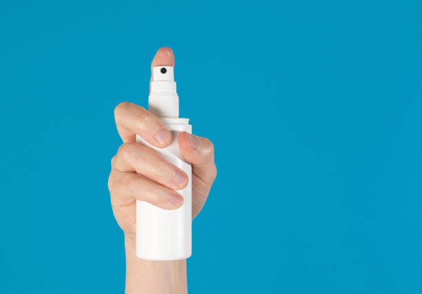 istock Hand holding up a white spray bottle, isolated against a blue background 1250013019