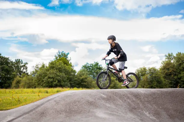 Young caucasian girl in sport clothes and a helmet on her head riding a bmx bicycle outdoors on the bicycle track.