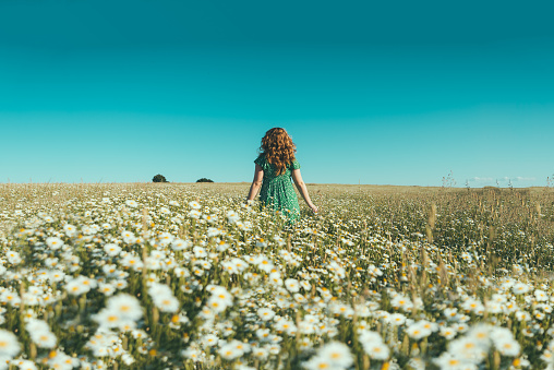 woman on her back with open arms in a field of daisies