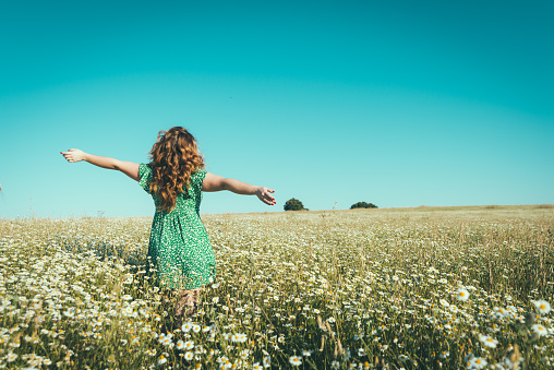 woman on her back with open arms in a field of daisies