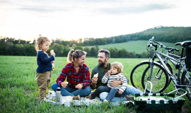 familia con dos niños pequeños en viaje en bicicleta, sentado en la hierba y descansando. - resting place fotografías e imágenes de stock