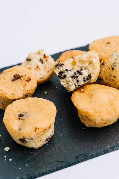 istock Little chocolate chips muffins with one bitten in a dark slate board plate isolated on white. Muffin, sweet and food concept. 1250019210