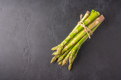 Bunch of fresh green asparagus is tied with a thread on dark graphite background top view with copy space
