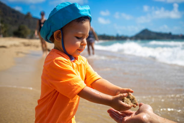 cute toddler in blue hat plays sand on the sea beach. close up stock photo
