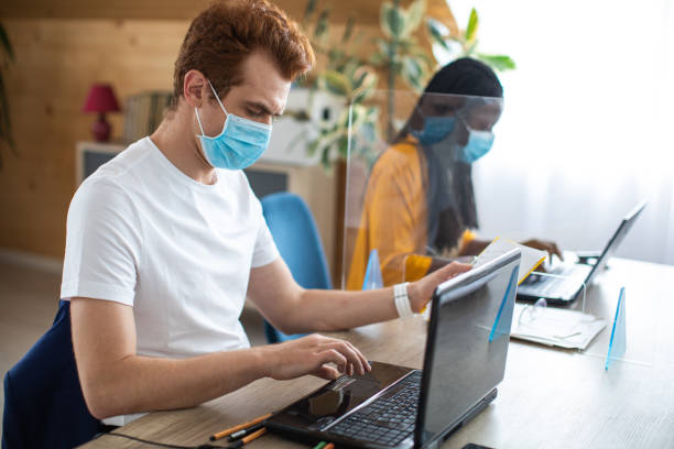 istock Colleagues with protective face masks using laptops at modern office 1250025592