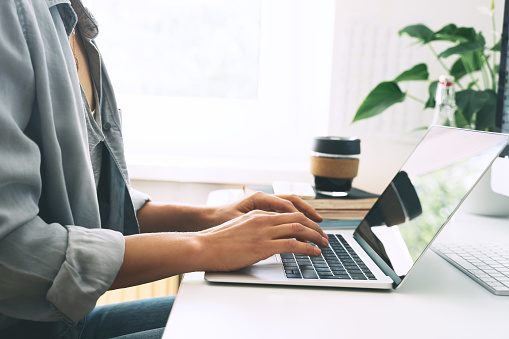 Primer plano de manos femeninas escribiendo texto en el teclado del ordenador portátil. Mujer trabajando o estudiando en la oficina en casa con una taza de café. Lugar de trabajo de freelancer. photo