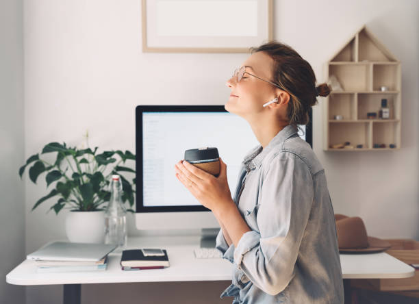 belle femme de sourire moderne travaillant et buvant le café de tasse réutilisable au bureau à la maison. - simplicity using computer women computer equipment photos et images de collection